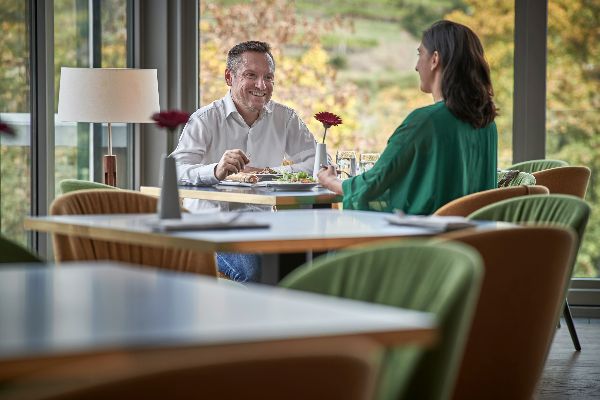 Ein Mann und eine Frau sitzen an einem Tisch in einem Lokal, im Vordergrund 2 leere Tische