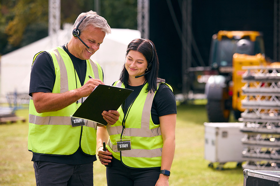 Eine Frau und ein Mann mit Headsets und Warnwesten gehen eine Checkliste durch.